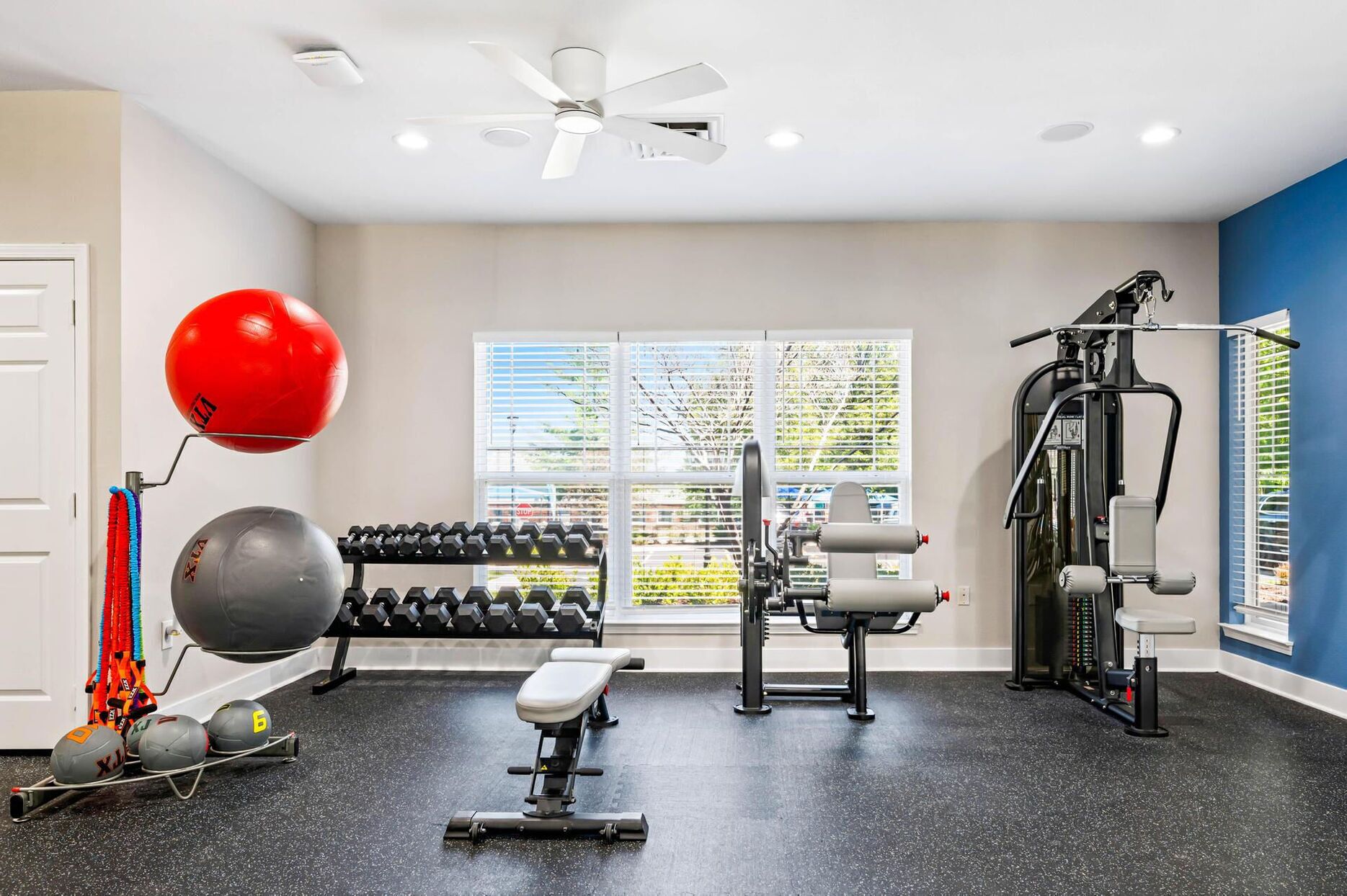 Un gimnasio con equipamiento de ejercicio, un ventilador de techo y una ventana con persianas.