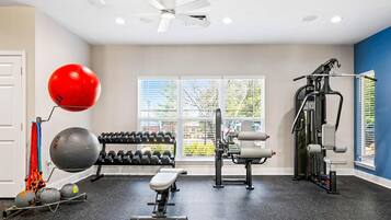Un gimnasio con equipamiento de ejercicio, un ventilador de techo y una ventana con persianas.