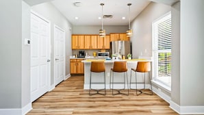 A modern kitchen with wooden cabinets, a stainless steel refrigerator, and a bar area with three stools. - Landing Apartments - Eureka (Eureka)