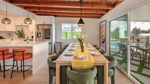 Una cocina moderna con vigas de madera, una isla central con taburetes de bar y un comedor con camino de mesa amarillo.