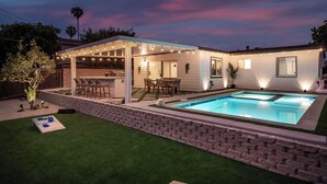 Un patio trasero con piscina, mobiliario de jardín y una zona de estar cubierta.