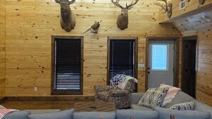 Interno di una baita in legno con soffitto in legno, teste di cervo appese, ventola a soffitto, divano e camino.