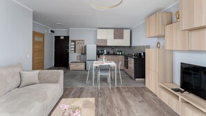 A modern living room with a sofa, a dining table, and a TV. - Osiedle Piastów Charming Apartment (Kraków)