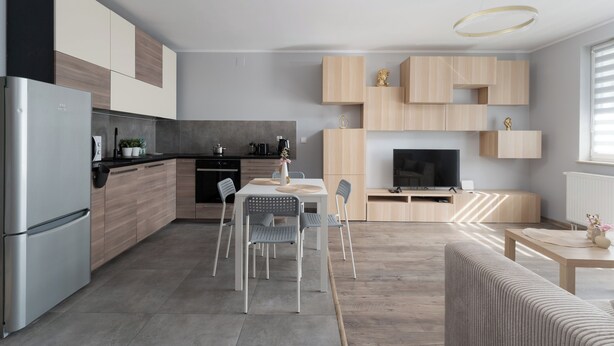 A modern kitchen with a dining area, built-in cabinets, a refrigerator, and a flat-screen TV. - Osiedle Piastów Charming Apartment (Kraków)