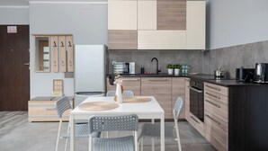 A modern kitchen with a white table and grey chairs, wooden cabinets, and a black countertop. - Osiedle Piastów Charming Apartment (Kraków)