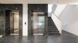 A modern elevator with marble walls and a staircase with wooden railings. - Krasiński Garden Deluxe Studio (Warszawa)