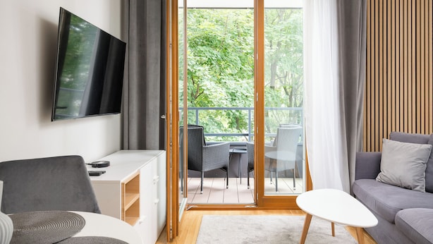A modern living room with a flat-screen TV, a grey sofa, a white coffee table, and a balcony with outdoor furniture. - Krasiński Garden Deluxe Studio (Warszawa)