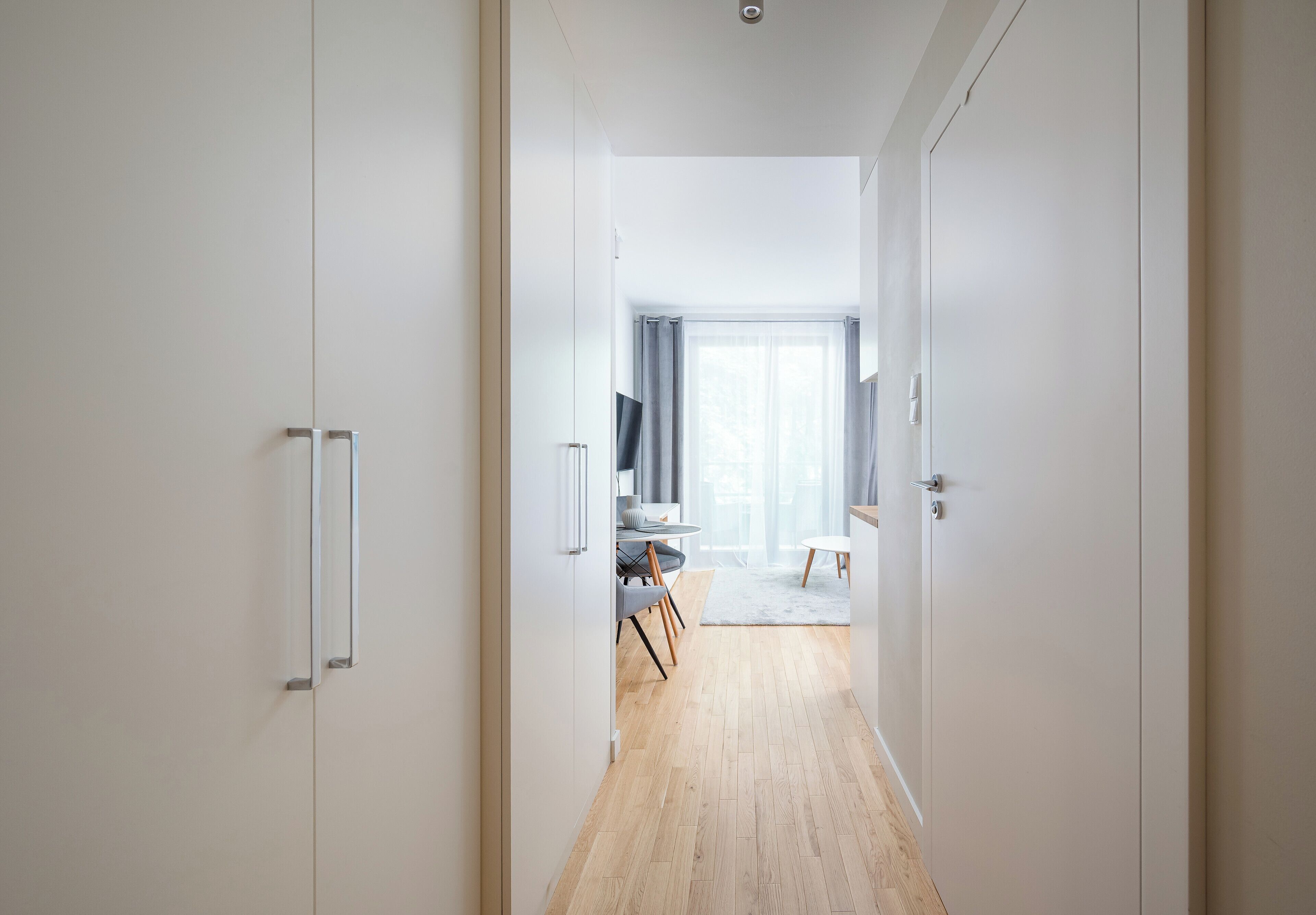 Un couloir mène à une salle à manger dotée d’un plancher en bois, d’une table à manger, de chaises et d’une fenêtre avec des rideaux.