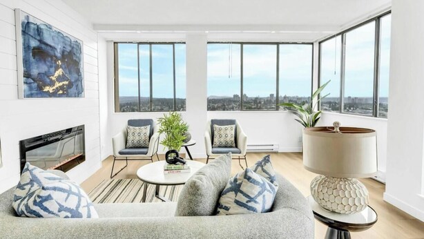 Una sala de estar moderna con chimenea, un sofá, dos sillones, una mesa de centro y un ventanal con vistas a la ciudad.