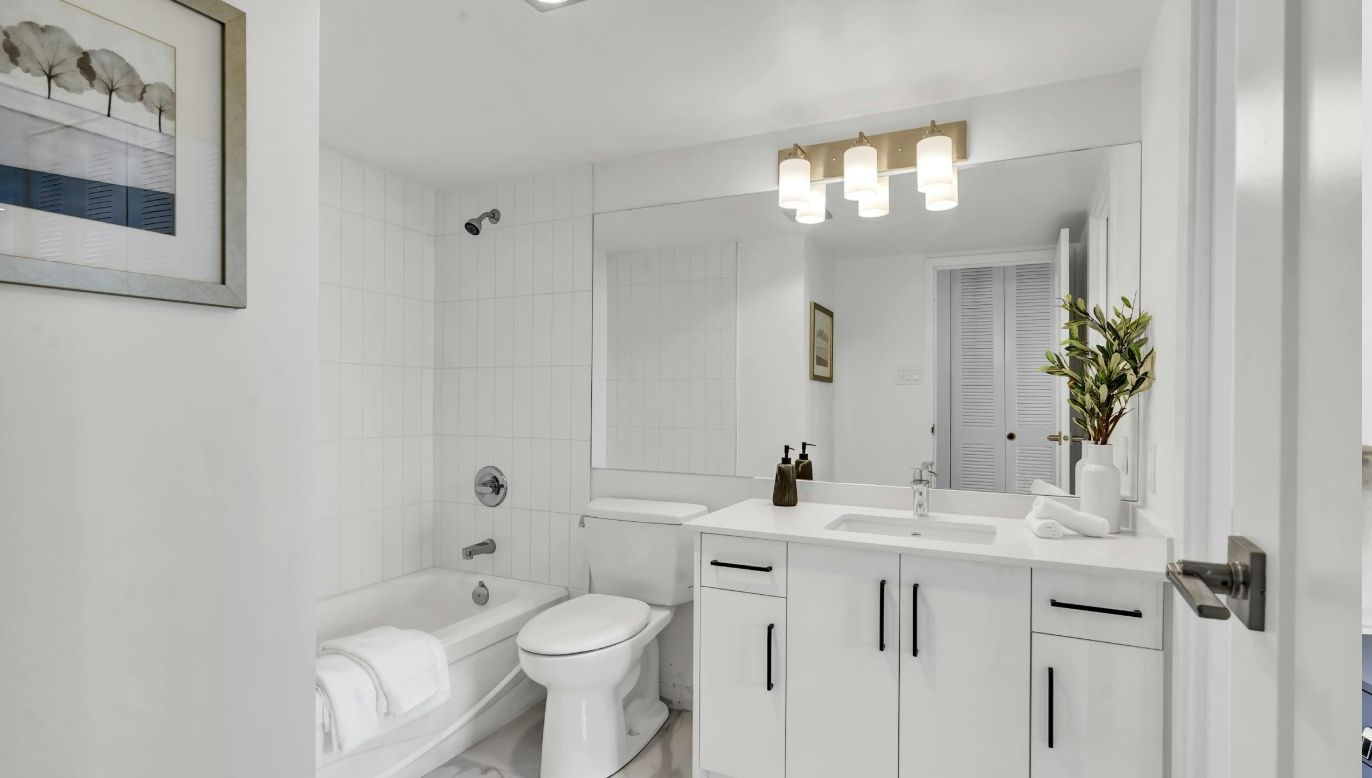 A modern bathroom with a white sink, toilet, and bathtub. There is a framed picture on the wall and a mirror above the sink.