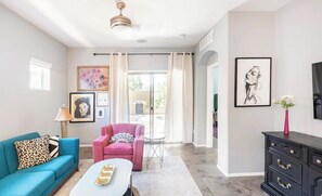 A living room with a blue sofa, a pink armchair, a white coffee table, and a black dresser. There are framed pictures on the walls and a ceiling fan. - Stylish 3BR/2BA in Gated Community-Walk to Westgate Entertainment District! (Glendale)