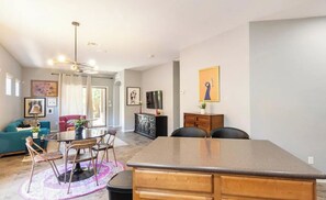 A modern living room with a dining area, a kitchen island, and a TV. There are framed pictures on the walls and a ceiling fan. - Stylish 3BR/2BA in Gated Community-Walk to Westgate Entertainment District! (Glendale)