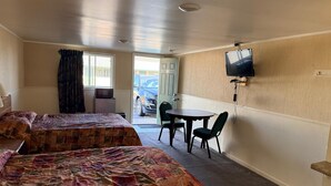 A hotel room with two beds, a small table with chairs, a television mounted on the wall, and a view of parked cars outside. - Tourest Motel (Peru)