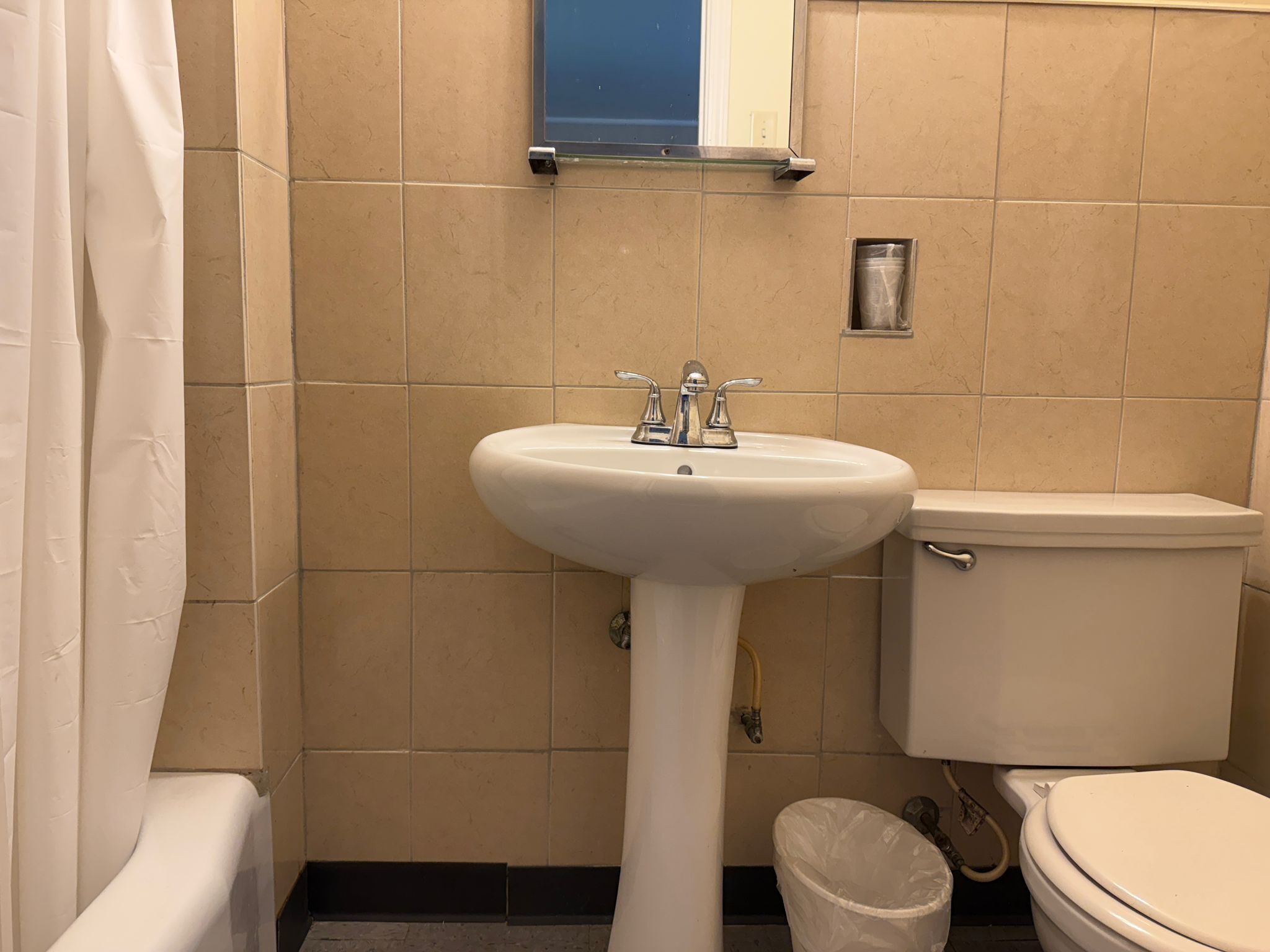 Un baño con lavamanos blanco, inodoro y un cubo de basura.
