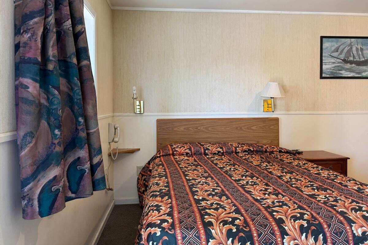 Une chambre d’hôtel avec une tête de lit en bois, une couvre-lit à motifs, une lampe de chevet et un tableau encadré au mur.