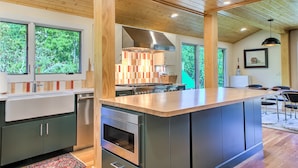 Une cuisine moderne dotée d’un îlot central, d’un plafond en bois et de grandes fenêtres.