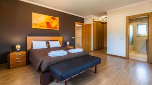 Une chambre à coucher moderne avec un grand lit, des lampes de chevet, un banc et un tableau au mur.