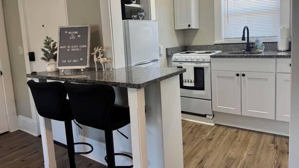 A kitchen with a central island, two bar stools, a refrigerator, a stove, and a window with blinds.