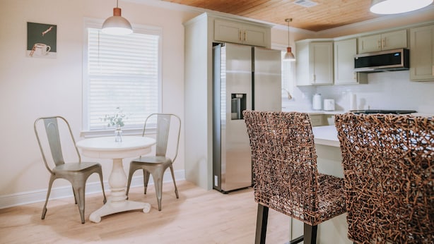 Una cocina moderna con armarios blancos, un refrigerador de acero inoxidable y una zona de comedor con dos sillas y una mesa.