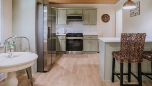 Una cocina moderna con armarios verde claro, electrodomésticos de acero inoxidable y techo de madera.
