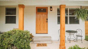 Una casa con puerta principal de madera, un pequeño porche con escalones, un banco y una mesa.