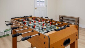 Una mesa de fútbolín en una habitación con piso de madera y una puerta blanca.