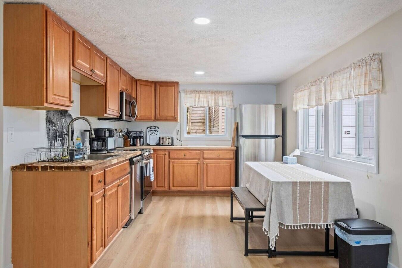 Una cocina compacta con armarios de madera, un refrigerador de acero inoxidable, un microondas y un lavamanos.