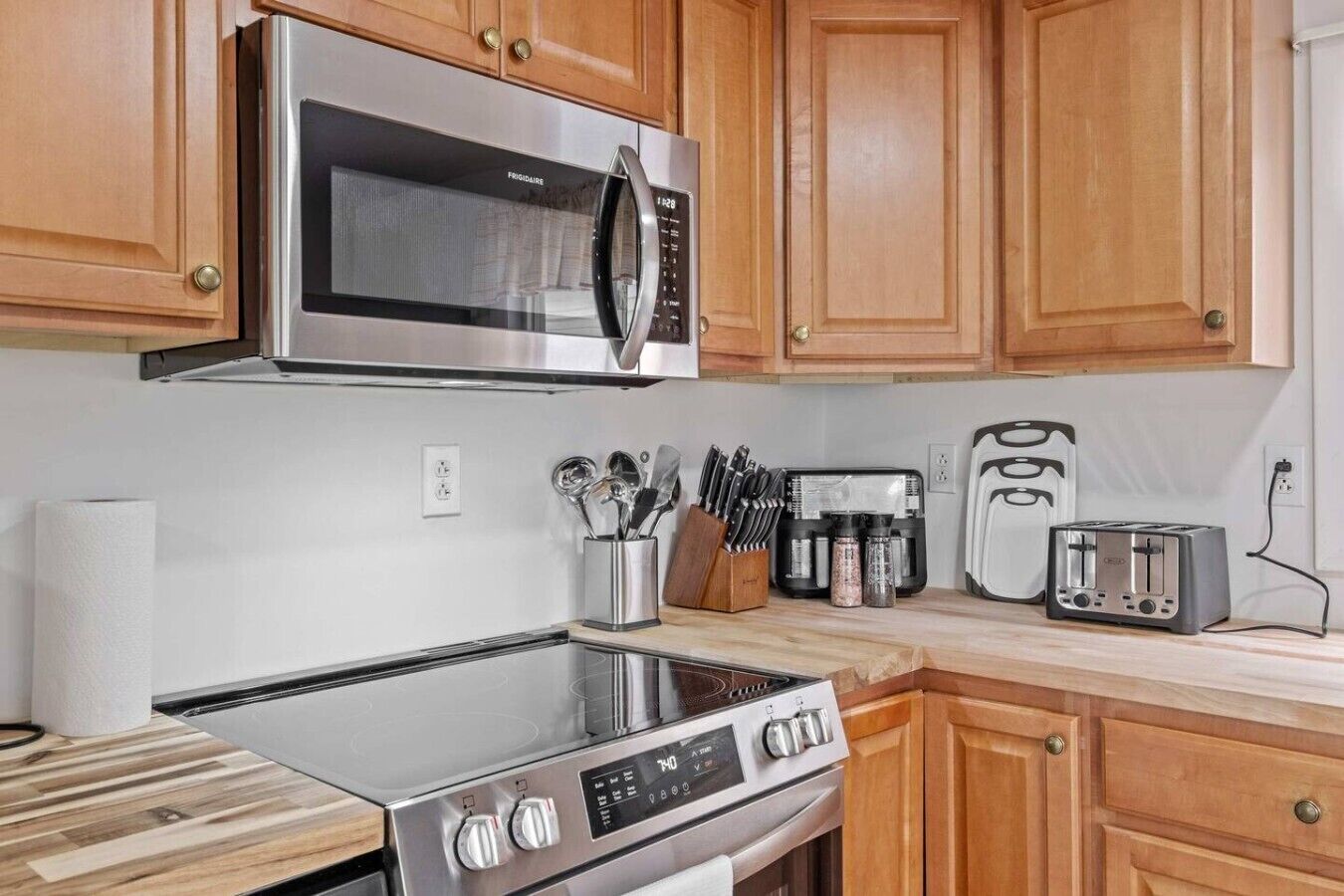 A kitchen with a stainless steel microwave, stove, toaster, and wooden cabinets.
