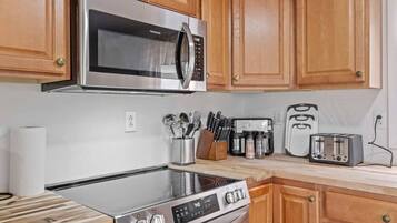 A kitchen with a stainless steel microwave, stove, toaster, and wooden cabinets.