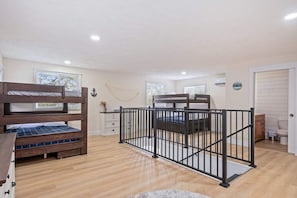 A bedroom with bunk beds, a small desk, a dresser, and a window with blinds.