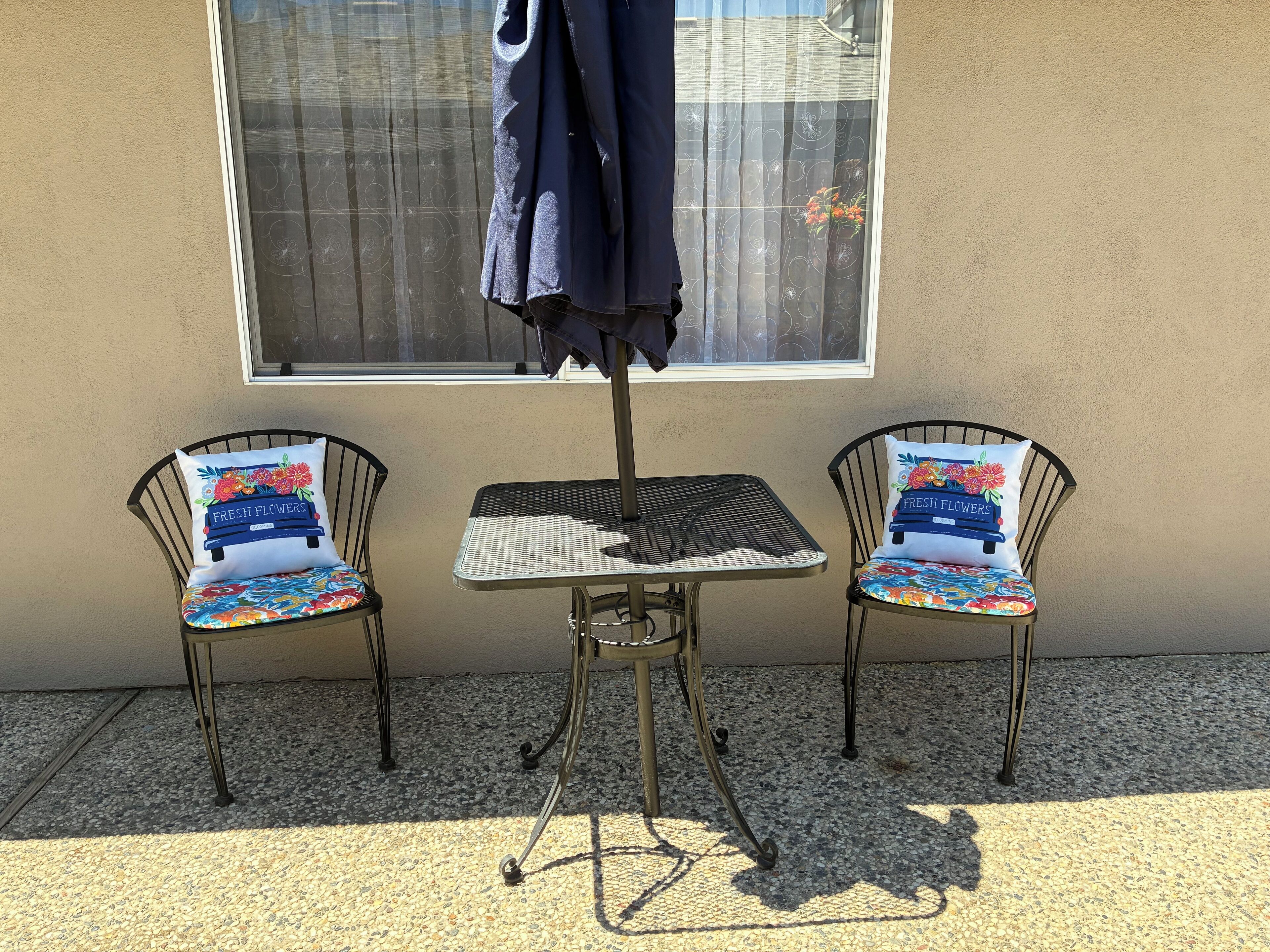 Two metal chairs with colorful floral cushions and a small metal table with a patterned cushion. An umbrella is attached to the table.
