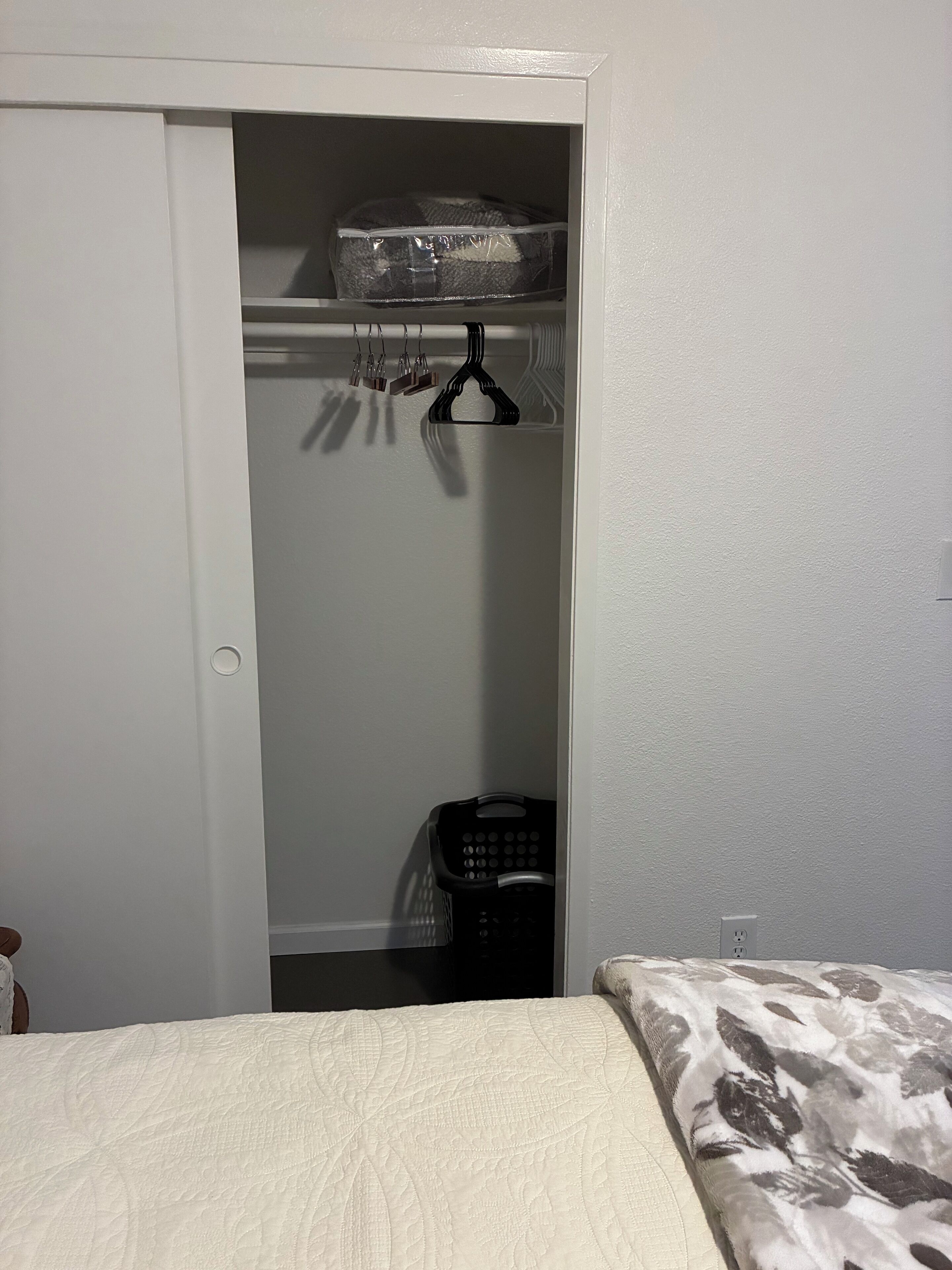 A bedroom with a bed, a closet with a hanging organizer, and a laundry basket.
