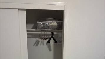 A bedroom with a bed, a closet with a hanging organizer, and a laundry basket.