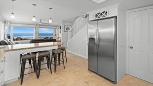 Een moderne keuken met een grote, roestvrijstalen koelkast, een bar met barkrukken, en uitzicht op de oceaan door het raam.