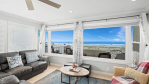Een woonkamer met uitzicht op het strand, een plafondventilator en een salontafel met decoratieve objecten.
