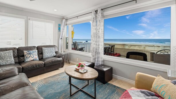 Een woonkamer met uitzicht op het strand, een plafondventilator en een bank met gestreepte kussens.