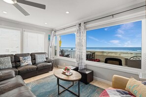 Ein Wohnzimmer mit Blick auf den Strand, einem Deckenventilator und einer Couch mit gemusterten Kissen.