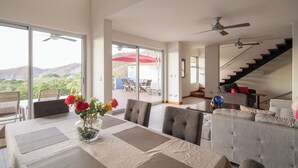 A spacious living area with a dining table set for four, a gray sofa, and a staircase leading to an upper level.