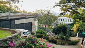 A residential area with a white car parked near a house, a person standing on a concrete staircase, and a garden with pink flowers.