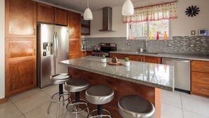 A modern kitchen with wooden cabinets, stainless steel appliances, a granite countertop, and bar stools.