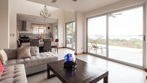 A spacious living room with a large sofa, a coffee table, and a view of the ocean through sliding glass doors.