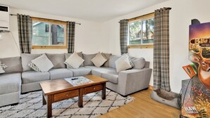 A living room with a grey sectional sofa, a wooden coffee table, and plaid curtains.