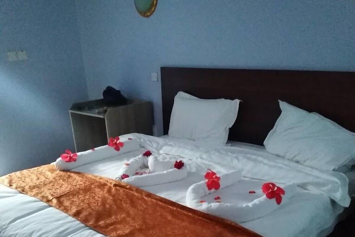 A hotel room with a neatly made bed, a brown throw blanket, and a headboard.