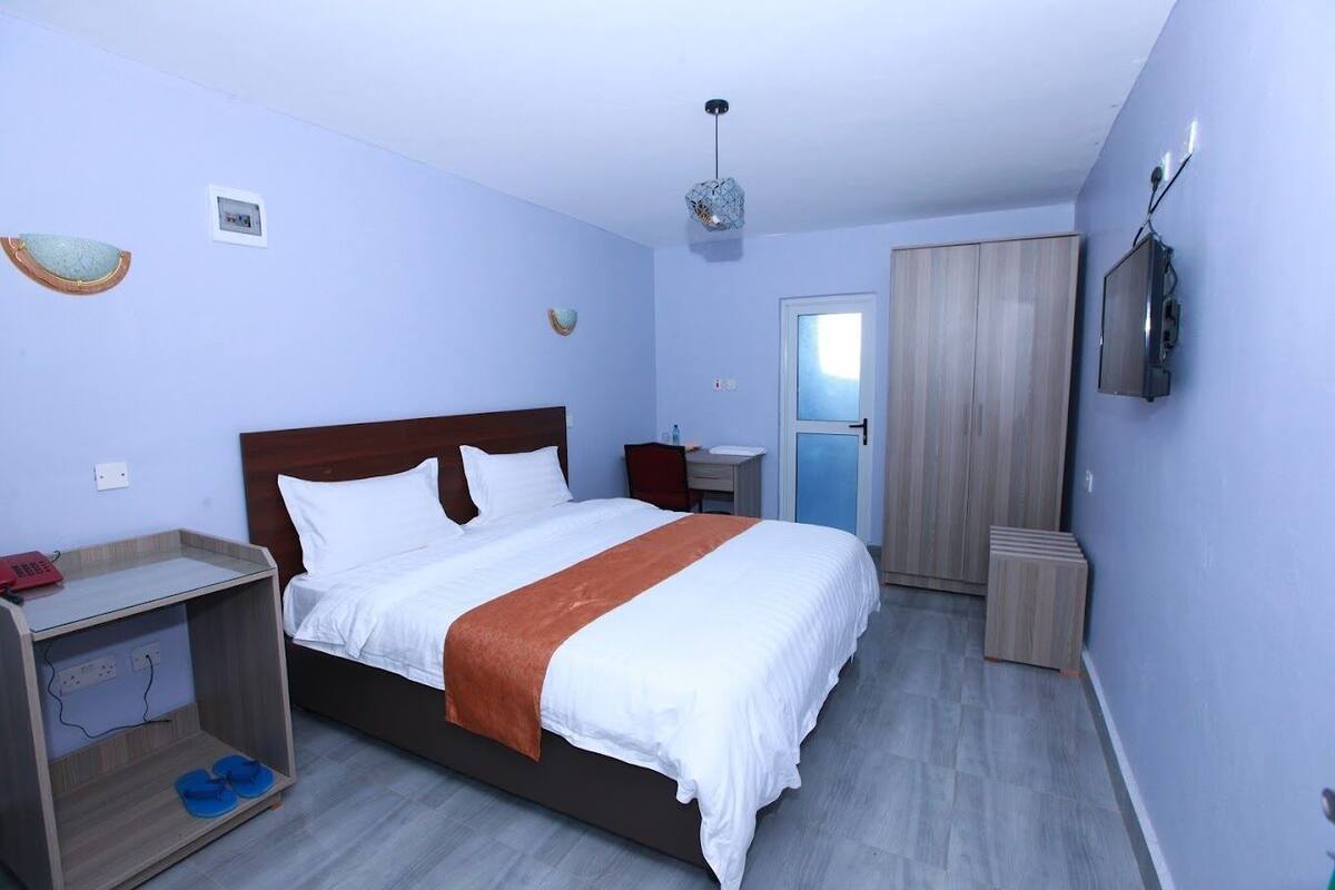 A bedroom with a bed, a desk, a wardrobe, and a TV.