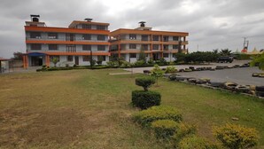 A multi-story building with a flat roof and balconies, surrounded by a grassy area with small bushes and a paved parking area with tires. - Eastern Ark Hotel (Nguluni)