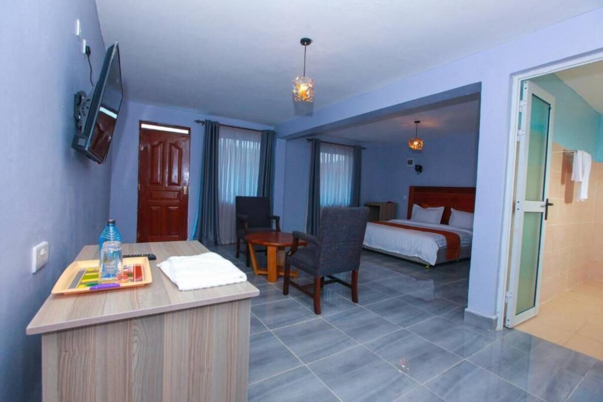 A hotel room with a bed, a desk with a chair, a TV mounted on the wall, and a door leading to another room.