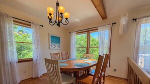 A dining area with a wooden table and chairs, a chandelier, and large windows with curtains. - Barefoot Manor - 4 BR home w/Private Pool, just a short distance from the beach (Southern Shores)