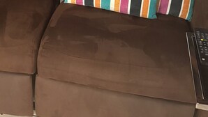 Un canapé marron avec un coussin à rayures, une télécommande et un escalier en arrière-plan.