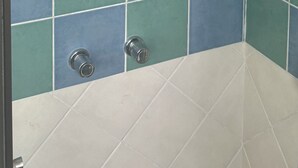 Une salle de bain avec un espace douche dont le mur est recouvert de carreaux blancs et bleus.