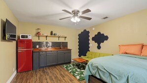 Une chambre à coucher de taille modeste, comprenant un lit, une table de chevet, un réfrigérateur rouge, un four à micro-ondes et un ventilateur de plafond.